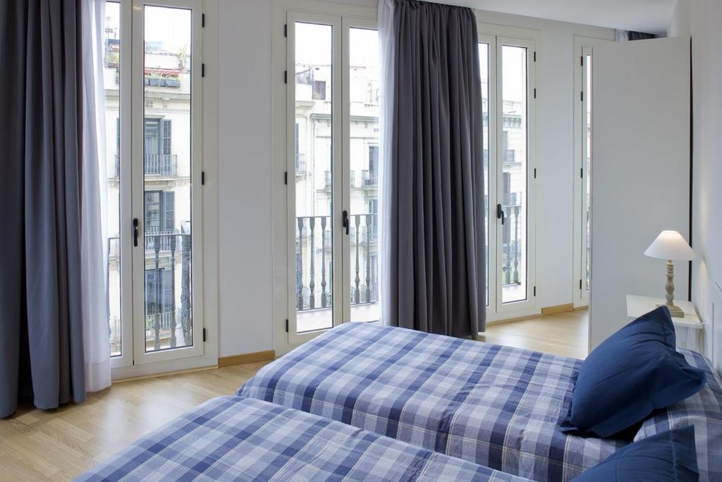 Flateli Pelai في برشلونة: غرفة نوم مع سرير مع الوسائد الزرقاء والنوافذ