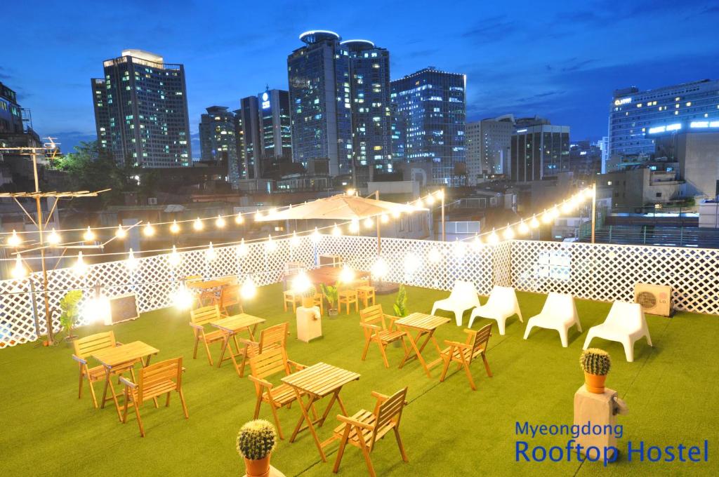 a rooftop patio with tables and chairs and a city skyline at OYO Rooftop Hostel in Seoul