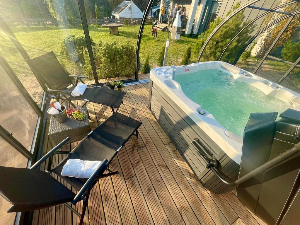 a hot tub sitting on a deck with two chairs at Osada Skoczkowo domki z kominkami, jacuzzi, balią i sauną nad jeziorem in Podiazy