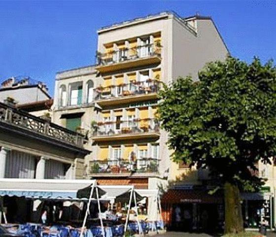 ein hohes weißes Gebäude mit einem Baum davor in der Unterkunft Hotel Elena in Stresa