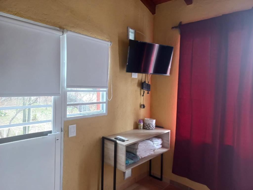 Habitación con cortina roja y mesa con TV. en Complejo Los Manantiales, en Alta Gracia