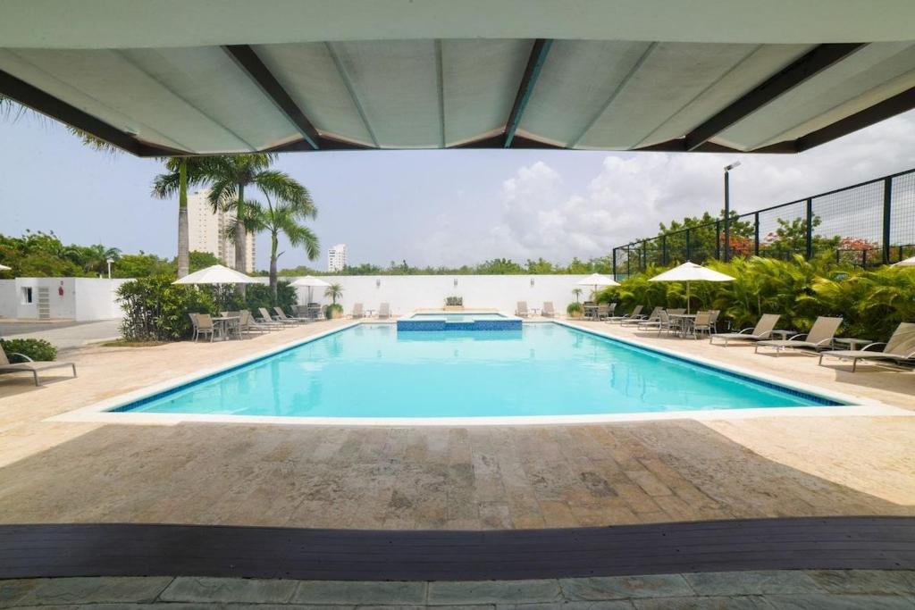 una gran piscina con sillas y sombrillas en Elegante Blue Marine Apartamento Juan Dolio, en Juan Dolio