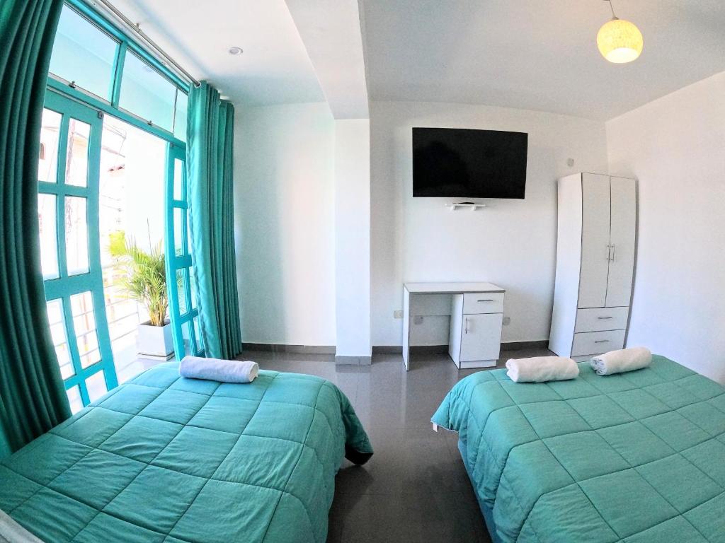 a bedroom with two beds and a tv and a window at AQUAMARINE PARACAS Beach Hostal in Paracas