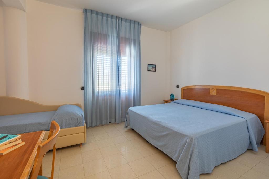 a bedroom with two beds and a table and a window at Hotel Sabbia d'Oro in San Vito lo Capo