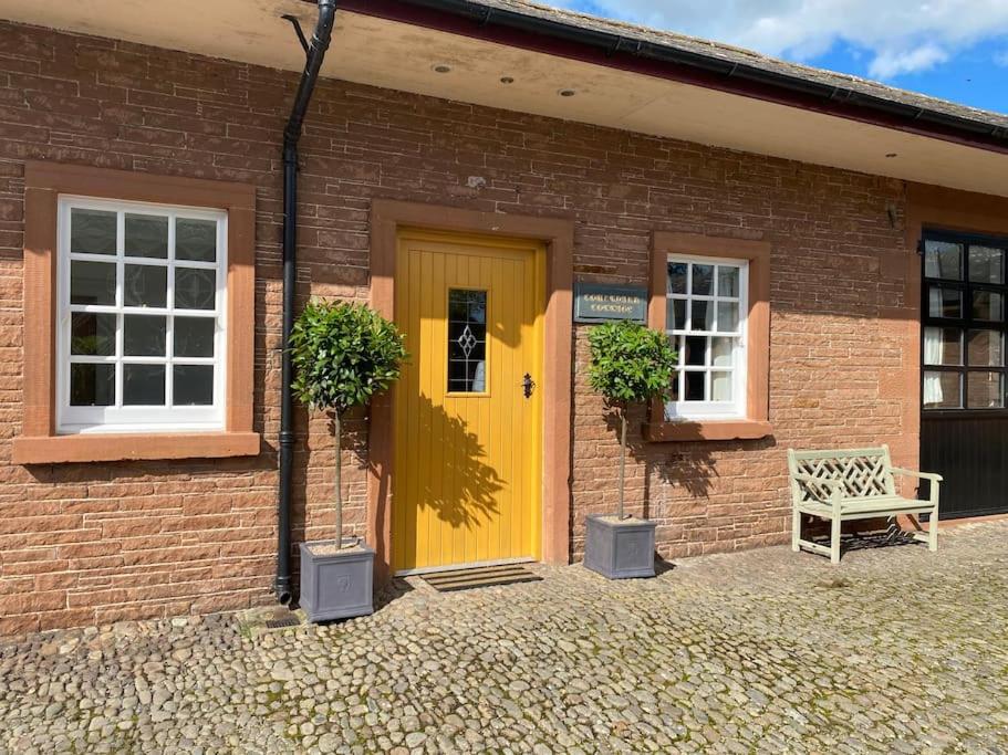 een gele deur op een bakstenen gebouw met een bank bij Courtyard Cottage in Lockerbie