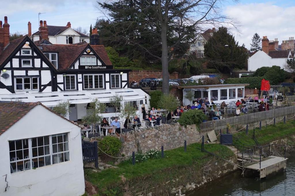 un grupo de personas sentadas fuera de un edificio junto a un río en Chandeliers 6 en Shrewsbury