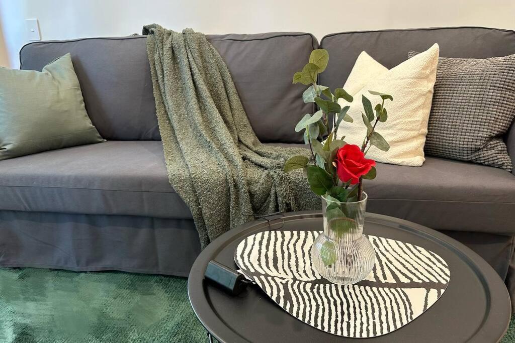 a vase with a red rose on a table in front of a couch at Brand New Luxe SOL Canberra CBD One bedroom Apartment in Canberra