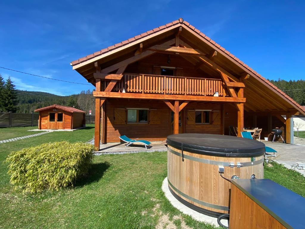 a large wooden cabin with a deck and a barrel at Le Chalet de la Devinière, bain nordique extérieur chauffé in Xonrupt-Longemer