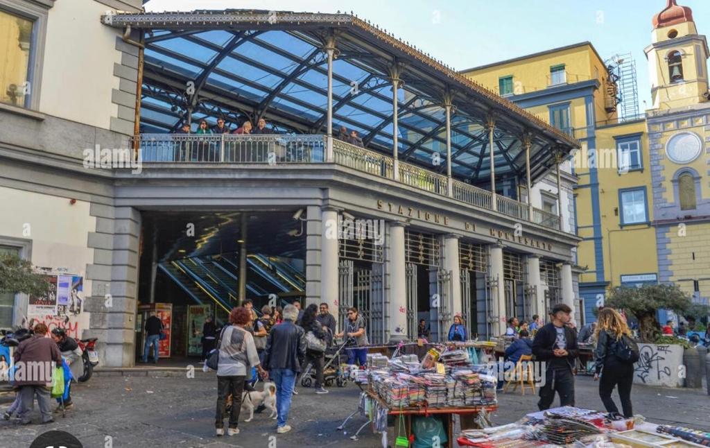 un gruppo di persone che camminano intorno a un mercato di fronte a un edificio di B&B La Cumana a Napoli