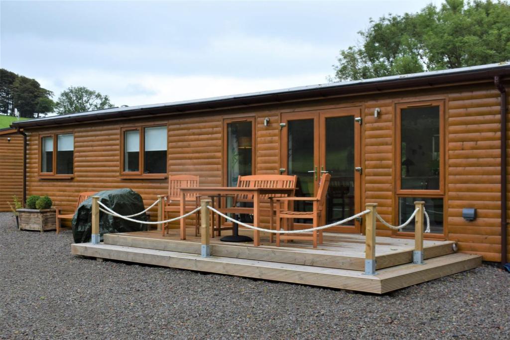 eine Holzhütte mit einer Terrasse mit Stühlen und einem Tisch in der Unterkunft Ridge View Lodge in Dumfries