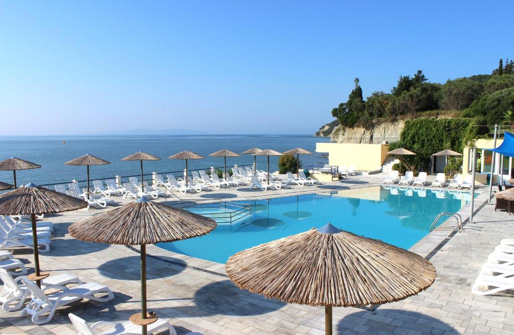 a swimming pool with chairs and umbrellas and the ocean at Ionian Sea View Hotel - Corfu in Kavos