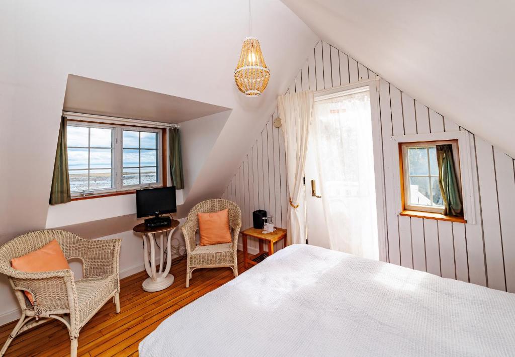 a bedroom with a white bed and chairs and a window at Auberge La Marmite in La Malbaie