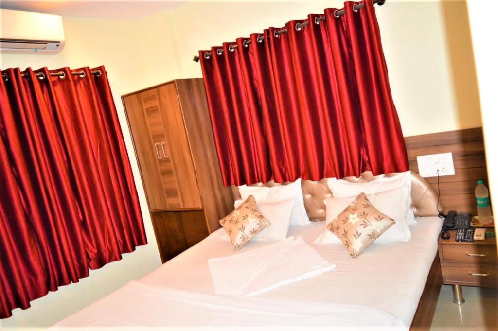 a bedroom with a bed with red curtains at Hotel Visau,Shirdi in Shirdi