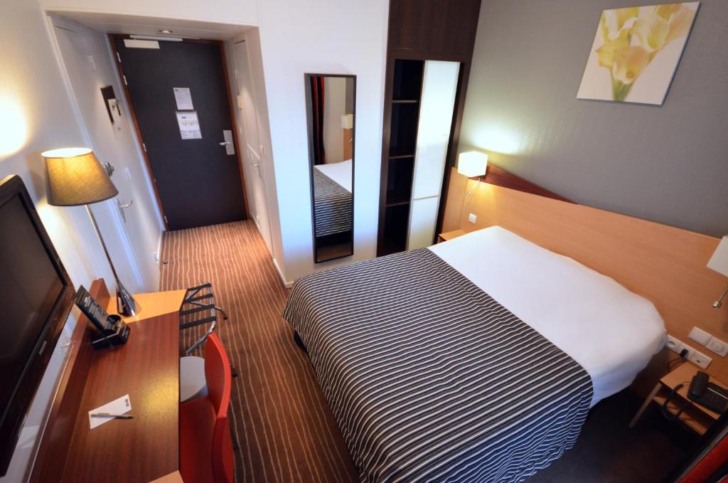 Habitación de hotel con cama, escritorio y TV. en Kyriad Hotel Dijon Gare, en Dijon