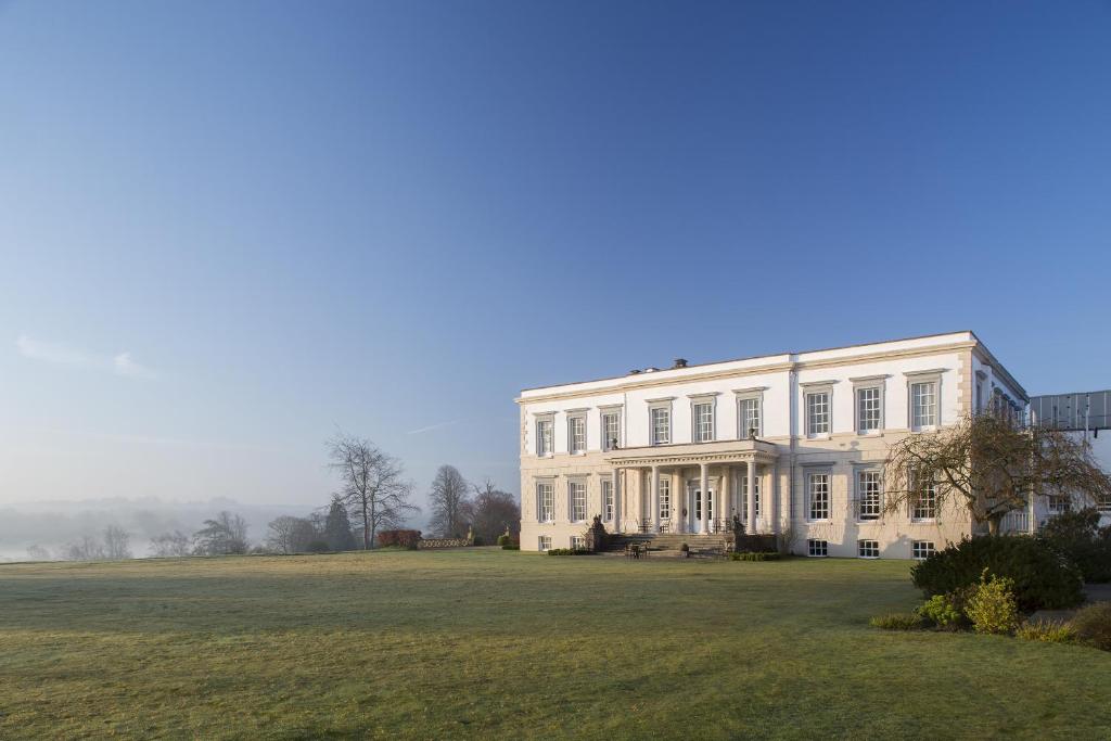 un grand bâtiment blanc sur une pelouse dans l'établissement Buxted Park Country House, à Buxted