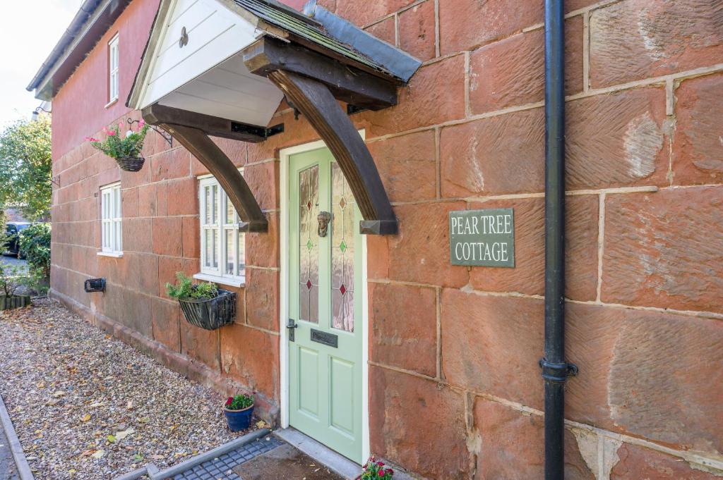 シュルーズベリーにあるPear Tree Cottageの緑の扉と看板が施されたレンガ造りの建物