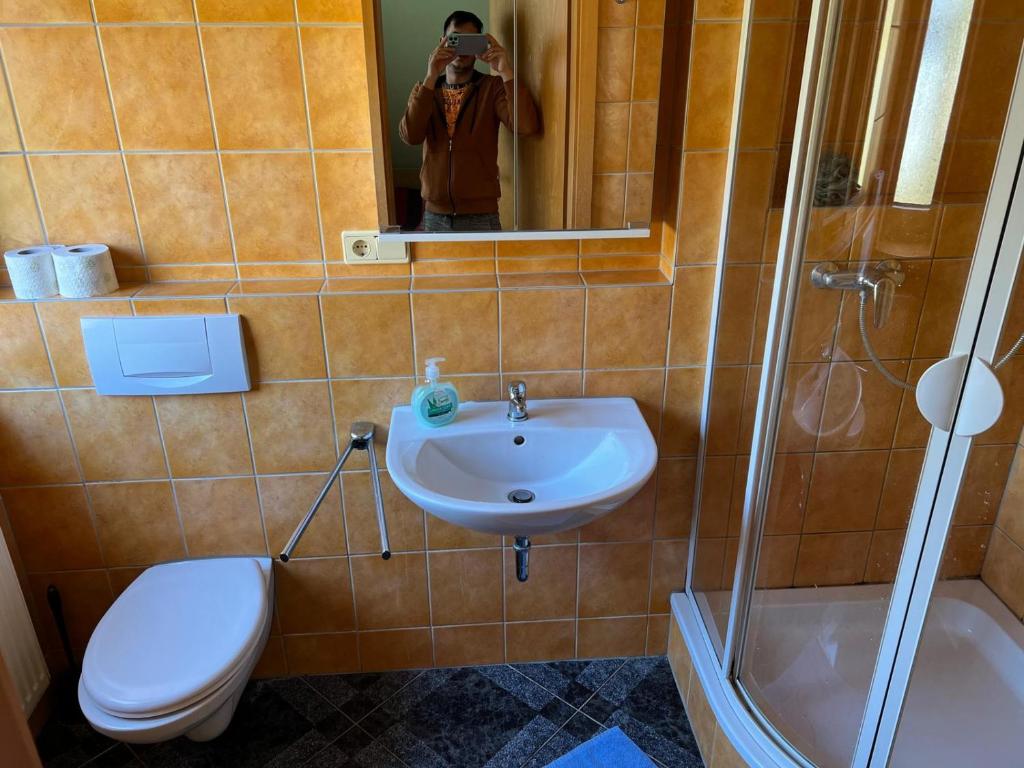 mężczyzna robiący zdjęcie łazienki z toaletą i umywalką w obiekcie Hotel Neue Krone w mieście Markt Erlbach