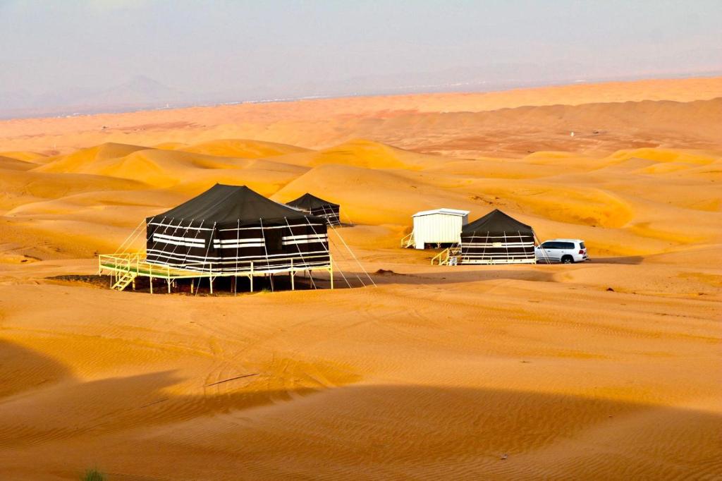 grupa namiotów na pustyni z białym samochodem w obiekcie Rashid Desert Private Camp w mieście Badīyah