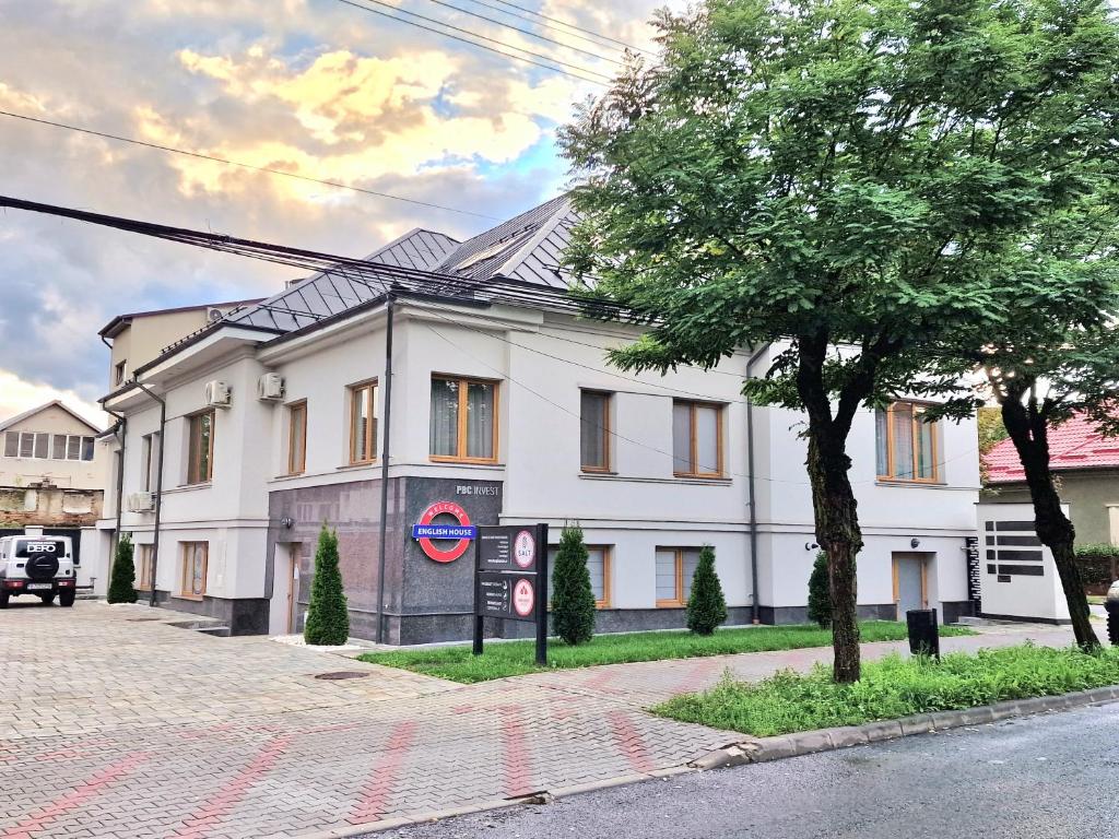 un edificio blanco con un árbol delante en English House, en Bistriţa