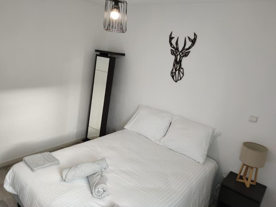a bed with white sheets and a clock on the wall at Spacieux et joli appartement de 2 à 4 personnes • Parking • Wifi in Fenouillet