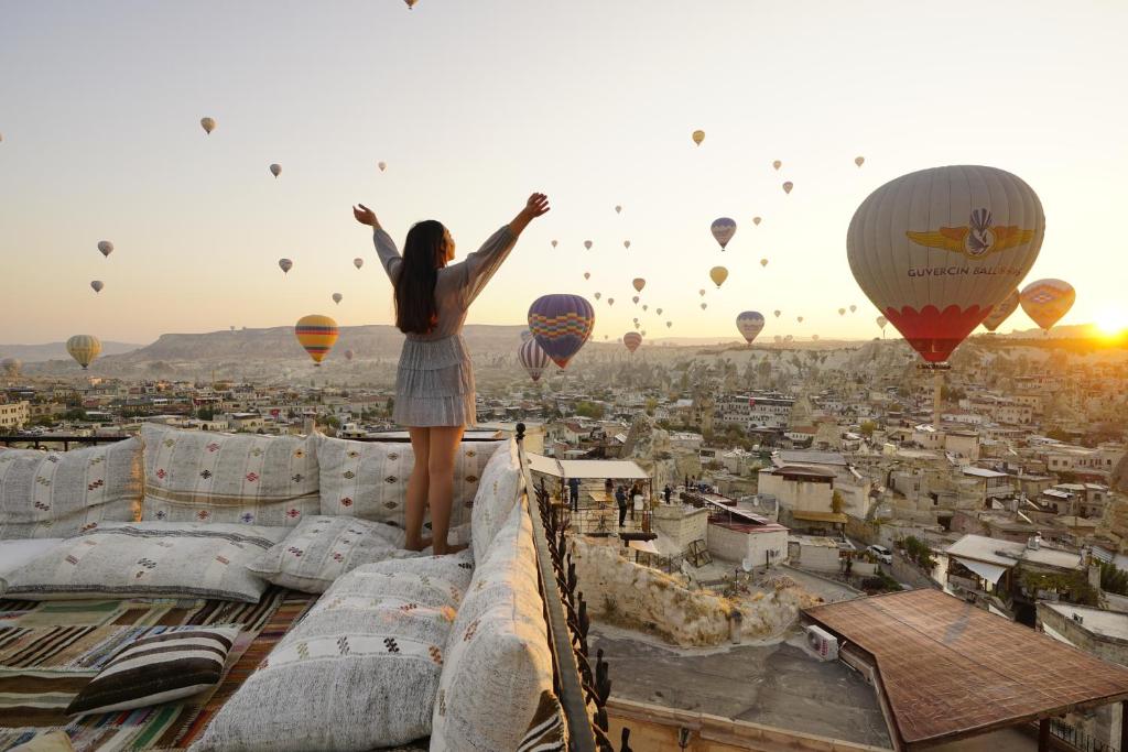Dziewczyna stojąca na dachu budynku oglądająca balony z gorącym powietrzem w obiekcie Tulip Cave Suites w Göreme