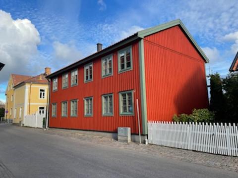 a red building with a white fence next to a street at Vadstena centrum in Vadstena