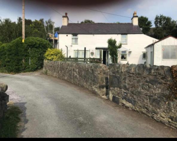 a house behind a stone wall next to a street at Bryn Pistyll 2 bedrooms Bethesda in Llanllechid