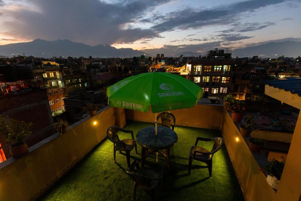 uma mesa e cadeiras numa varanda com um guarda-sol verde em Bhrikuti Stay em Patan