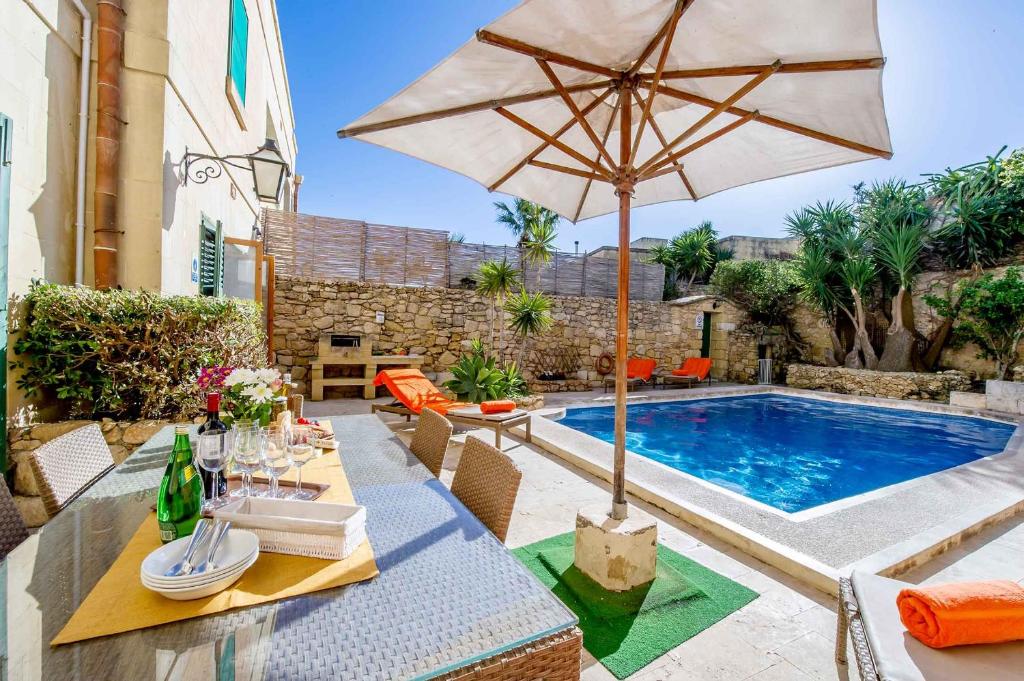 a patio with a table with an umbrella and a pool at Djar Ta Menzja 3 Holiday Home in Sannat