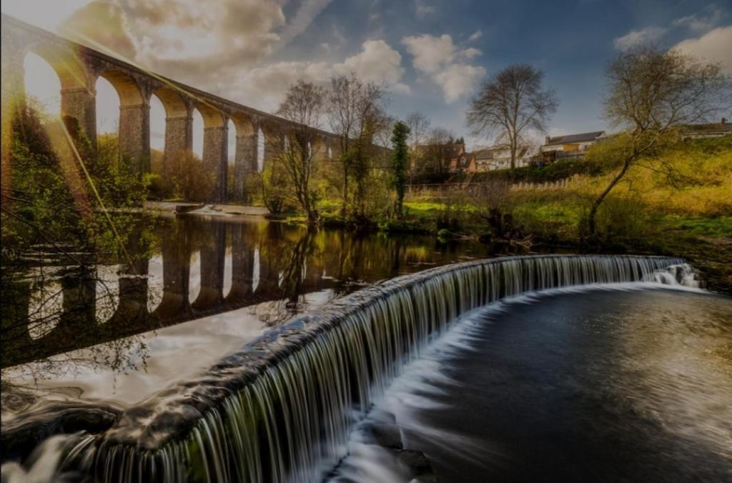 eine Brücke über einen Fluss mit einem fließenden Wasserfall in der Unterkunft Viaduct View - Cefn Coed in Merthyr Tydfil