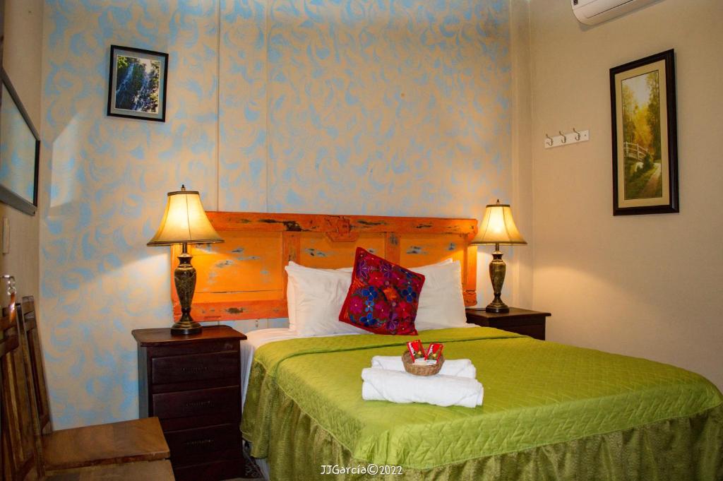 a bedroom with a bed with a green blanket and two lamps at Hostal Koltin Suchitoto in Suchitoto