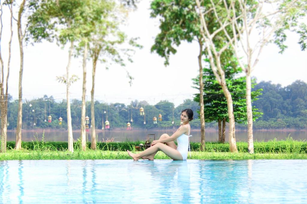 uma mulher sentada à beira de um corpo de água em River Tree Resort em Chiang Khan