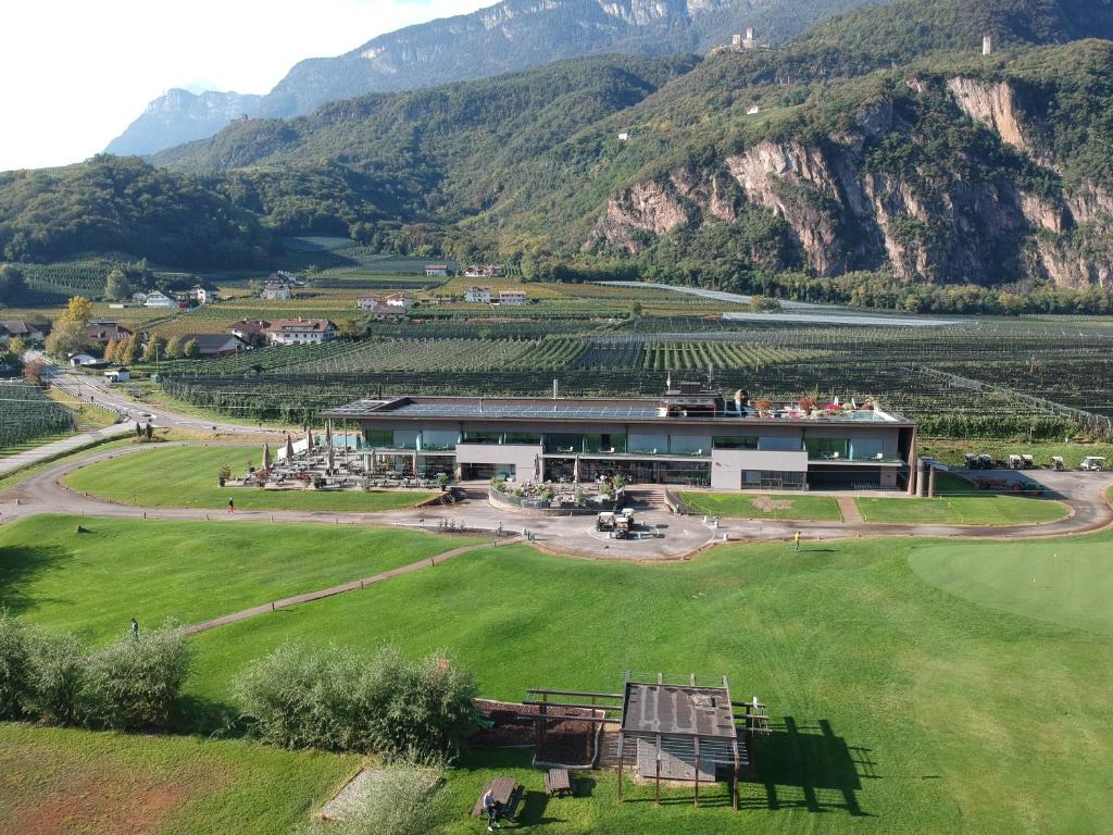 um edifício num campo com montanhas ao fundo em The Lodge Sporthotel - Golfclub Eppan em Appiano sulla Strada del Vino