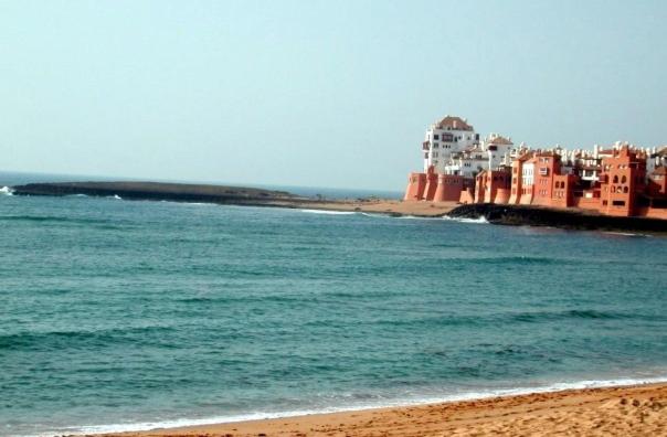 a beach with a group of buildings and the ocean at Soleil & Piscine BOUZNIKA in Bouznika