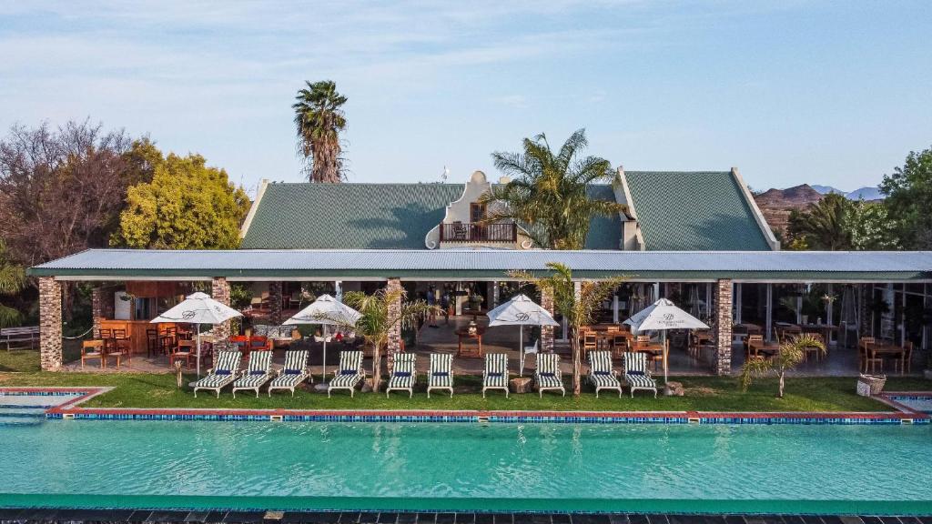 a resort with a pool and chairs and a building at Mooiplaas Guesthouse in Oudtshoorn