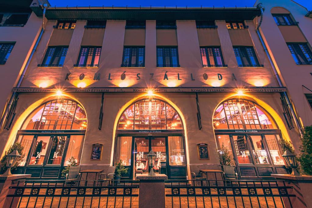 ein Gebäude mit beleuchteten Fenstern und Tischen davor in der Unterkunft Komló Hotel Gyula in Gyula