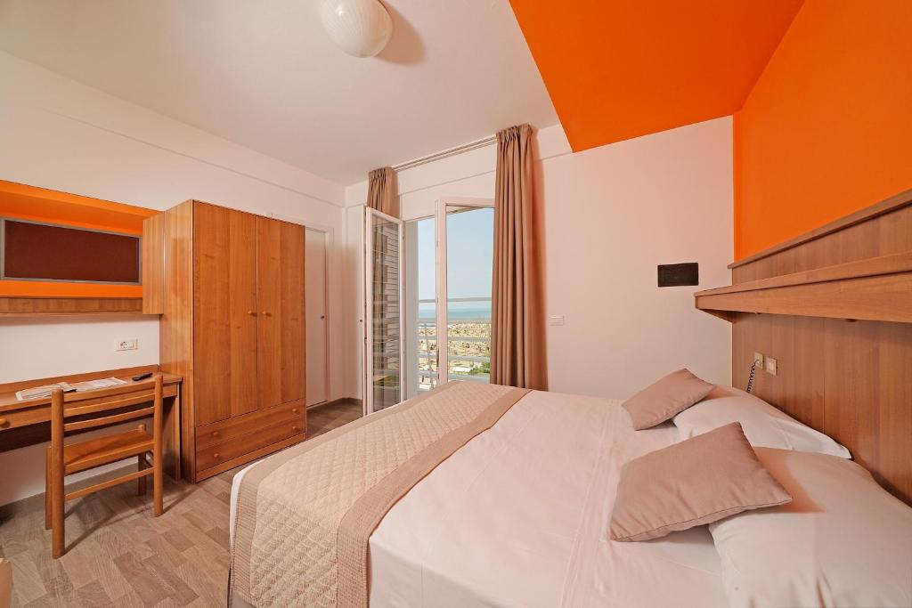 a bedroom with a bed and a desk and a window at Hotel Strand a frontemare in Lido di Jesolo