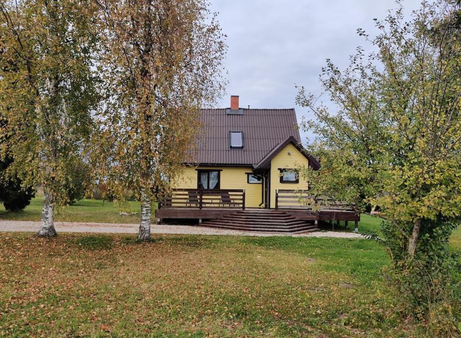 a yellow house with a porch in a field at Ilvese Cottage Lintsi jõe kaldal 
