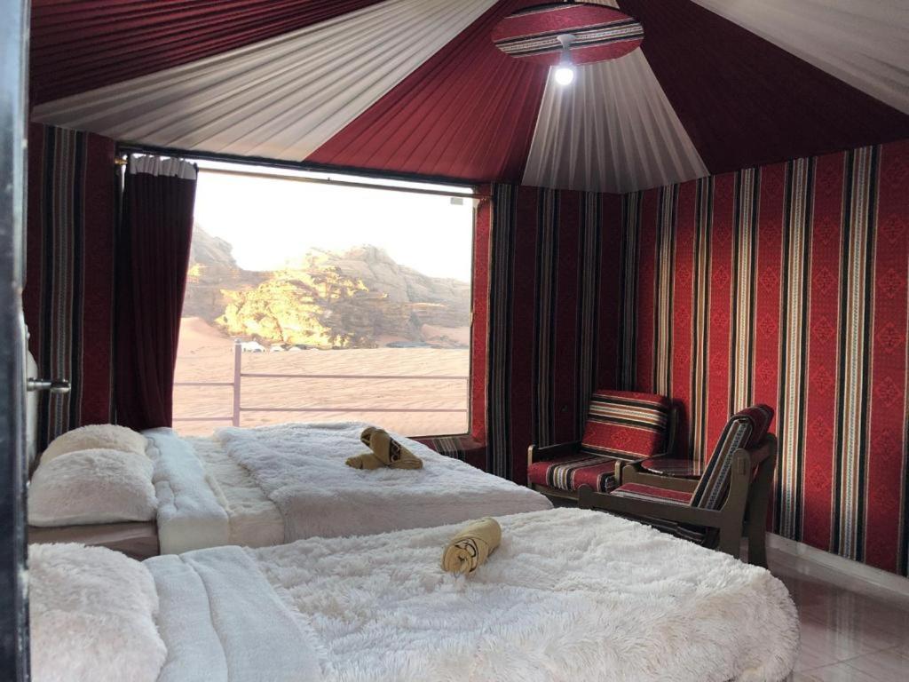 two beds in a room with a large window at Blue Camel in Wadi Rum