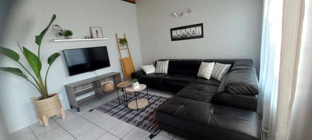 a living room with a black leather couch and a flat screen tv at Mucha Airbnb in Walvis Bay