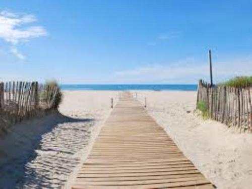 un chemin en bois à travers le sable sur une plage dans l'établissement Maison en bord de mer, à Mauguio