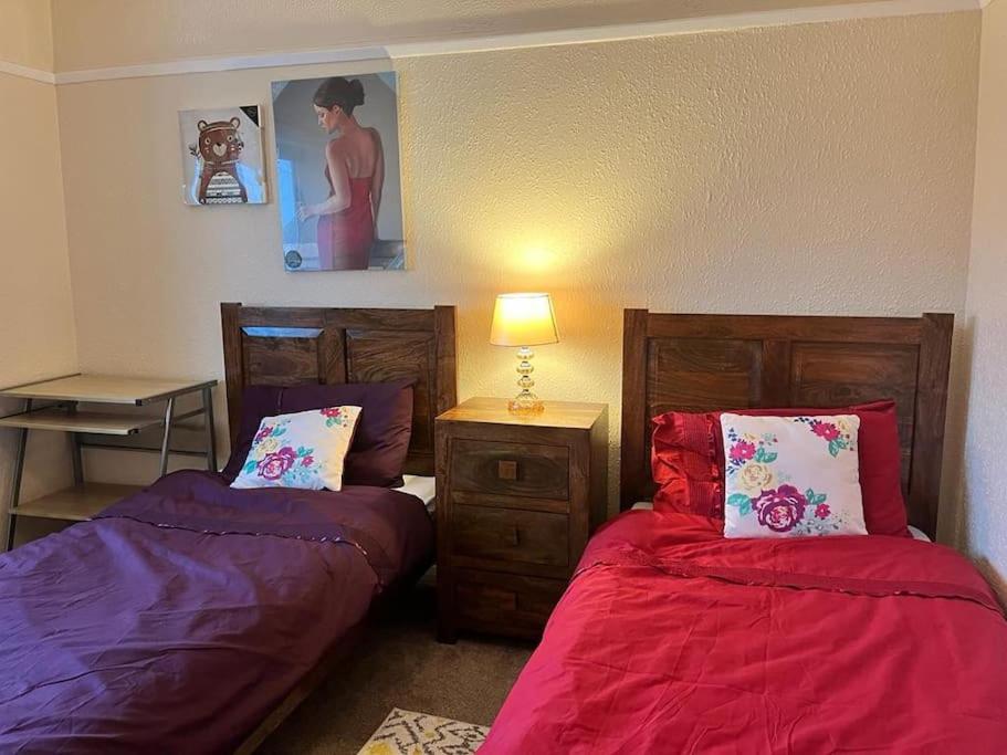 a bedroom with two beds with red sheets and a lamp at North Wales Holiday Accomodation with Free parking & WiFi in Bodelwyddan