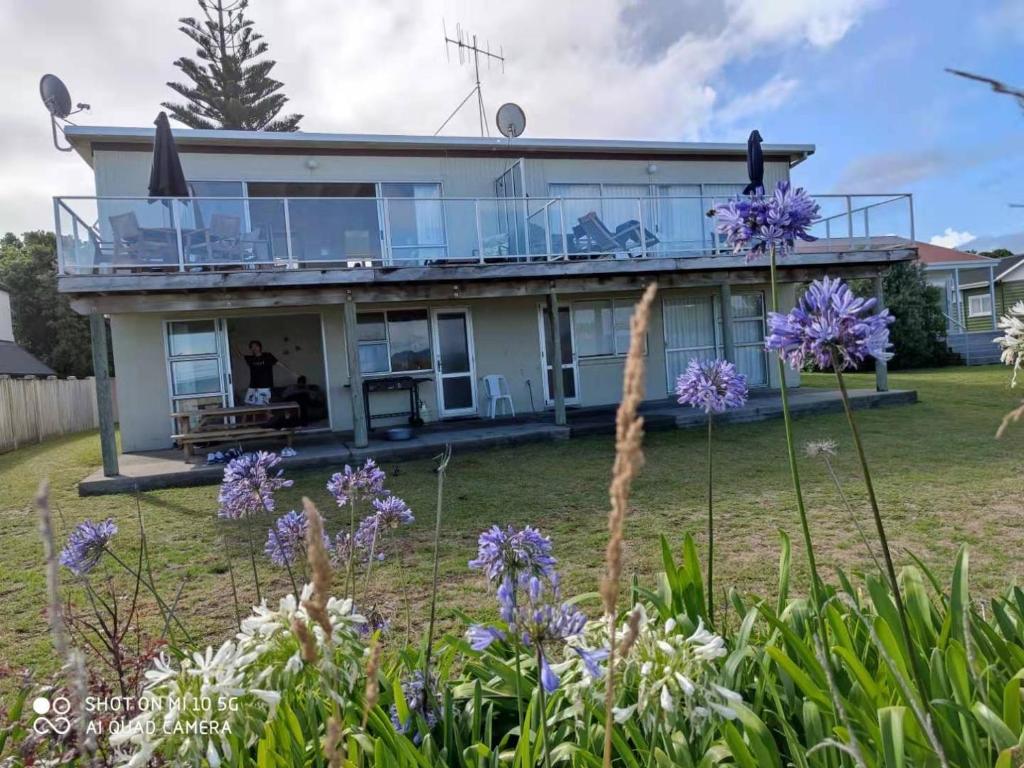 a house with a balcony and purple flowers at Hosts on the Coast Paradise on Pipi in Whangamata
