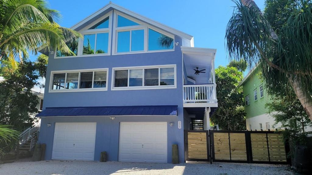 una casa azul con dos puertas de garaje y una valla en KL Retreat 6BR-4BTH with Jacuzzi and family room! en Key Largo