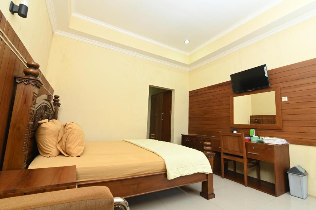 a bedroom with a bed and a desk and a television at MCM HOTEL WISATA BOJONEGORO in Bojonegoro