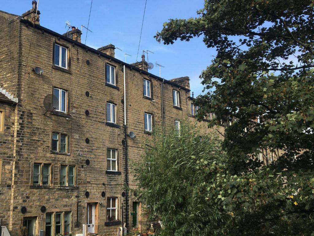 un vecchio edificio in mattoni con finestre bianche e un albero di Up-Top Cottage a Holmfirth