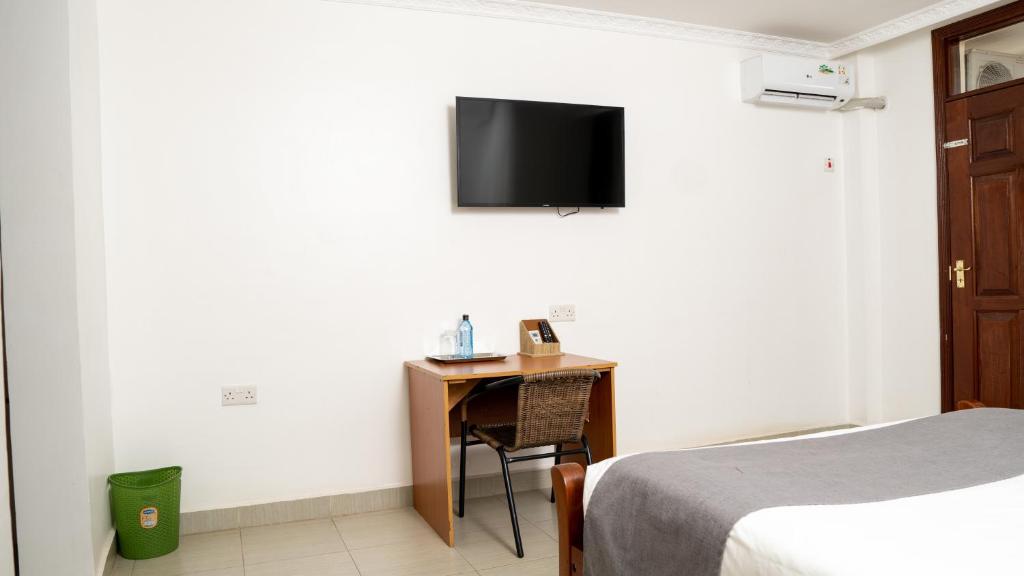 a room with a bed and a desk with a tv on the wall at Whirlspring Hotel in Kisumu