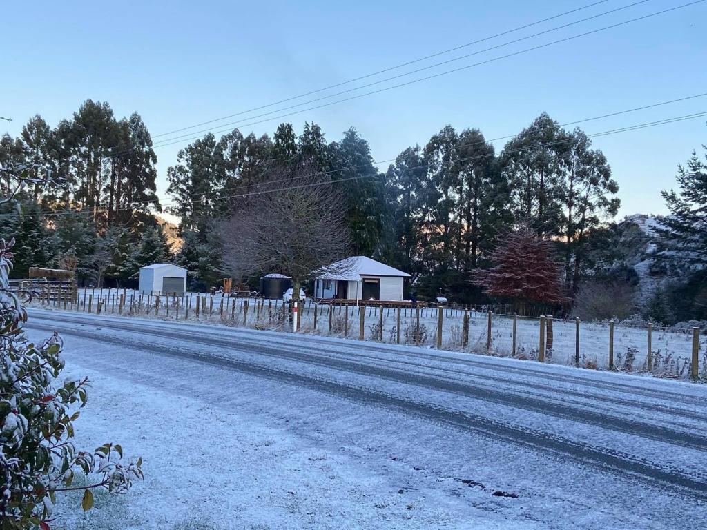 uma estrada coberta de neve com uma cerca e uma casa em Cosy Country Cottage - Outdoor Pizza Oven - Rural Setting on 4 Acres em Raetihi