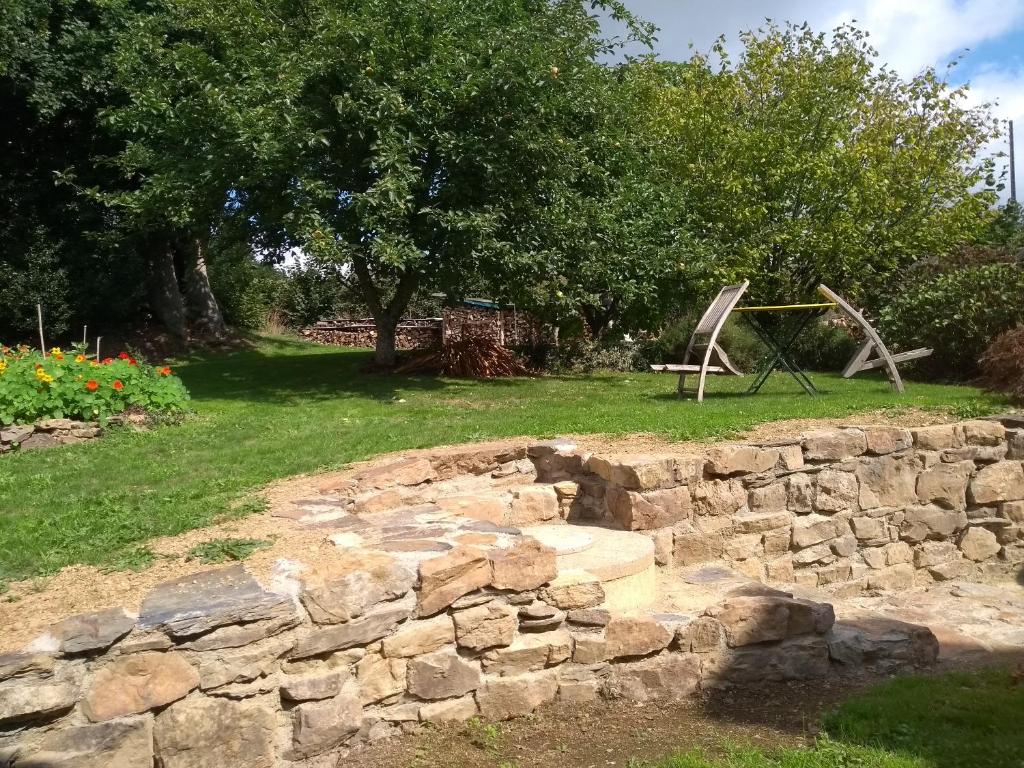 een stenen muur in een tuin met een boom en een schommel bij Chaleureuse maisonnette in Lopérec