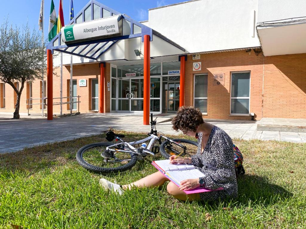 Eine Frau, die mit einem Laptop im Gras sitzt. in der Unterkunft Albergue Inturjoven Sevilla in Sevilla